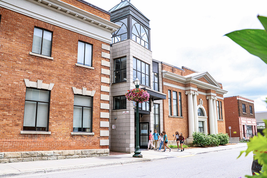 A historic building of red brick with a glass and steel entrance and people entering. The Mill Street Library in Orangeville, Ontario.